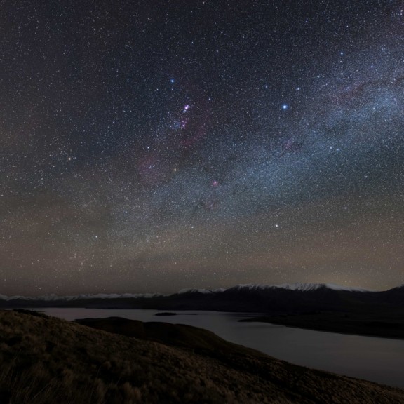View across Lake Tekapo to snowcapped mountains with milky way